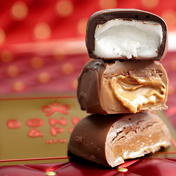 A red chocolate tin with an assortment of individually wrapped chocolates, including pretzels, nuts, and cookies, displayed after opening.