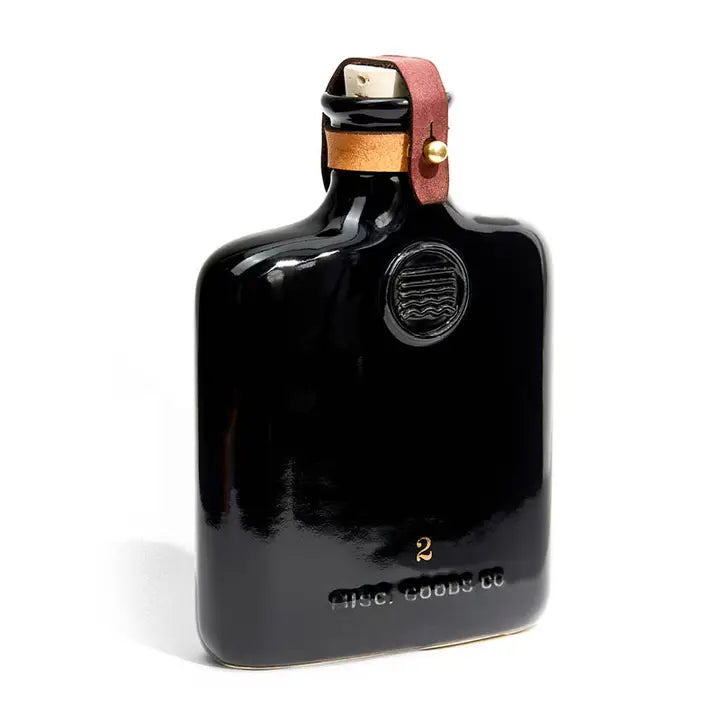 Classic ceramic flask inspired by the historic culture of distilling spirits, featuring intricate embossing, leather fastening, and brass hardware. Perfect for casual picnics, bar tops, or mantles.