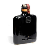 Classic ceramic flask inspired by the historic culture of distilling spirits, featuring intricate embossing, leather fastening, and brass hardware. Perfect for casual picnics, bar tops, or mantles.
