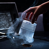 Hand holding a crystal whiskey glass with smoke, showcasing a premium barware experience for scotch and bourbon enthusiasts.