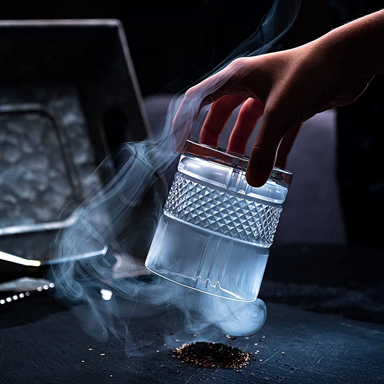Hand holding a crystal whiskey glass with smoke, showcasing luxury barware for whiskey enthusiasts.