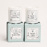 Two candles in boxes labeled 'Yacht Club' and 'Little Black Bag' on a white background