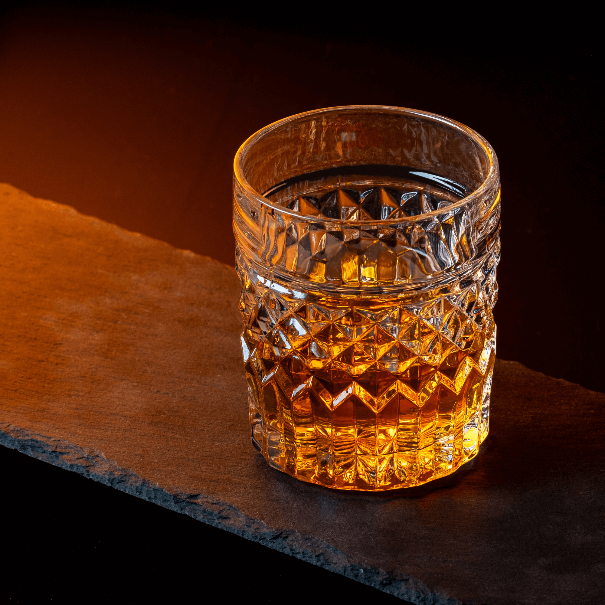 Crystal whiskey glass filled with golden whiskey on a dark slate background, perfect for cocktails and spirits.