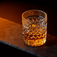 Crystal whiskey glass filled with golden whiskey on a dark slate background, perfect for cocktails and spirits.