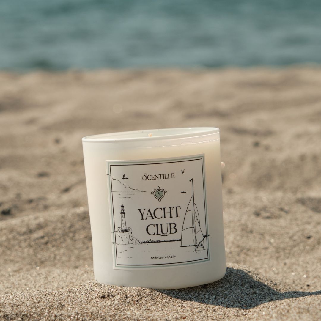 Candle labeled 'Yacht Club' on a sandy beach with ocean in the background