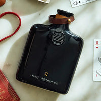 Classic ceramic flask inspired by the historic culture of distilling spirits, featuring intricate embossing, leather fastening, and brass hardware. Perfect for casual picnics, bar tops, or mantles.