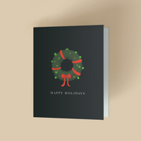 A dark green holiday greeting card featuring a festive winter wreath tied with a red ribbon at the bottom, centered above the text "HAPPY HOLIDAYS" in gold lettering, set against a warm beige background.