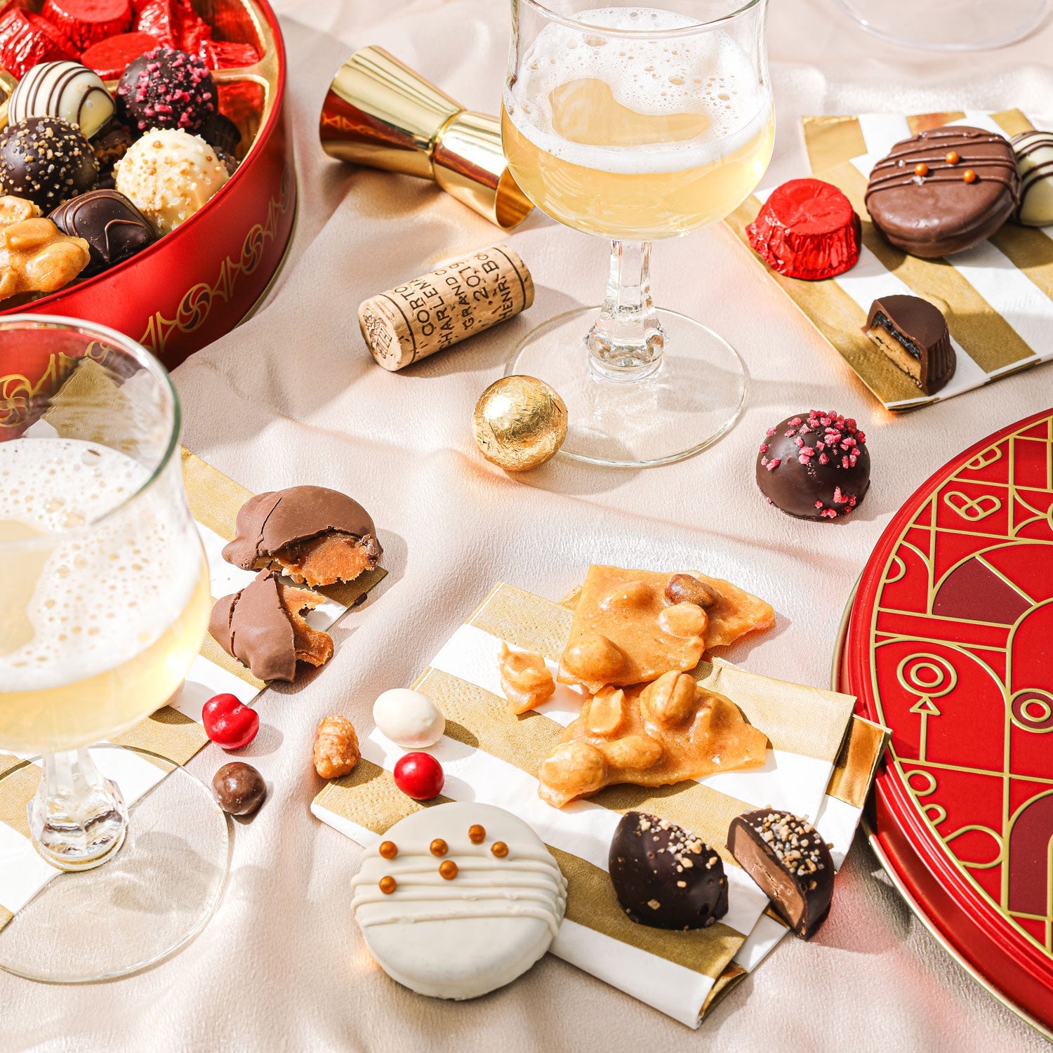 A festive red and gold circular box of assorted gourmet sweets including chocolate covered treats, nut clusters, and candy balls.