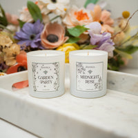 Two candles labeled 'Garden Party' and 'Midnight Rose' on a marble surface with flowers in the background.