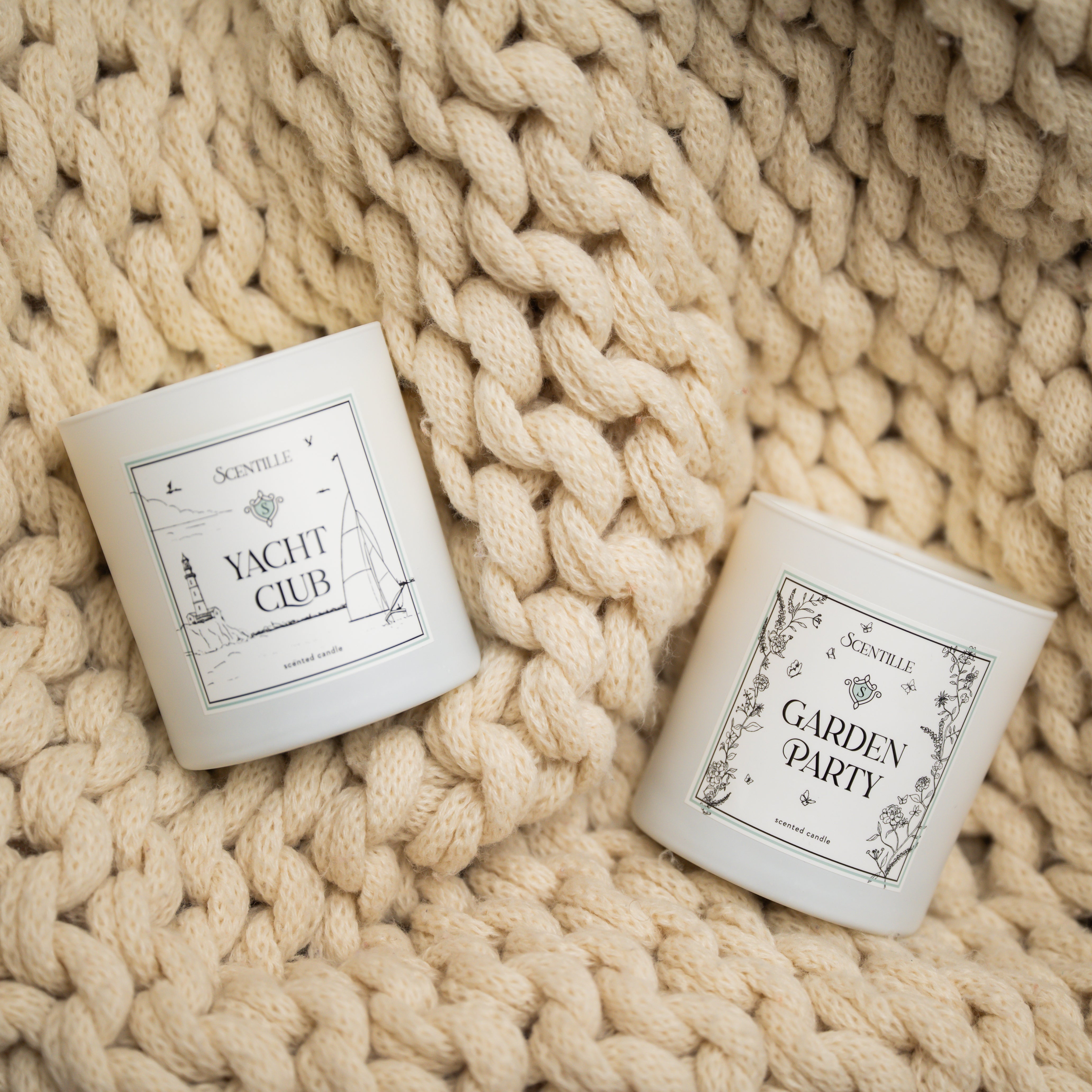 Two candles labeled 'Yacht Club' and 'Garden Party' on a textured beige surface.