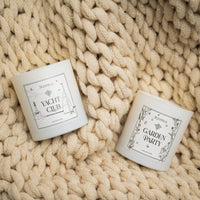Two candles labeled 'Yacht Club' and 'Garden Party' on a textured beige surface.