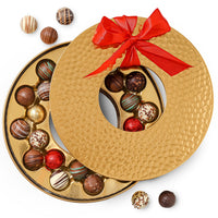 A round gold box with a red ribbon on top, filled with assorted chocolate candies and truffles.